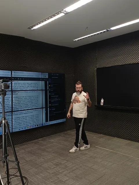 Professor no estúdio ao lado da televisão com um texto aberto